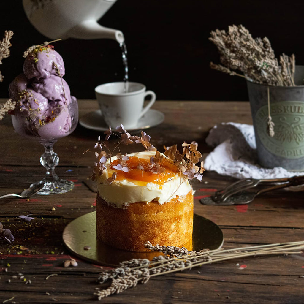 Small cake with white frosting and orange filling on a wooden table with lavender and a teapot.
